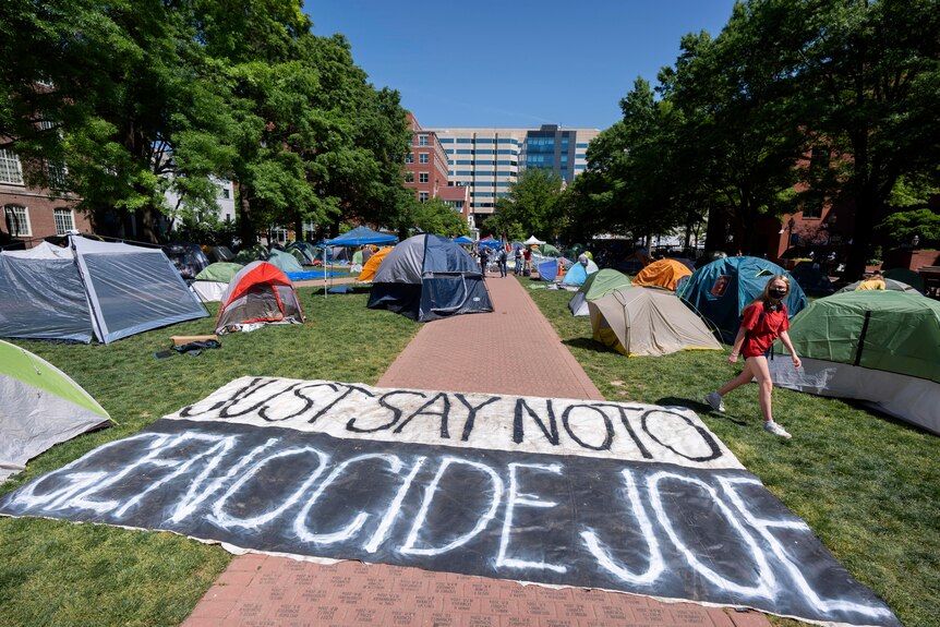 A banner on the ground that reads 'Just say no to genocide joe' with tents around it.