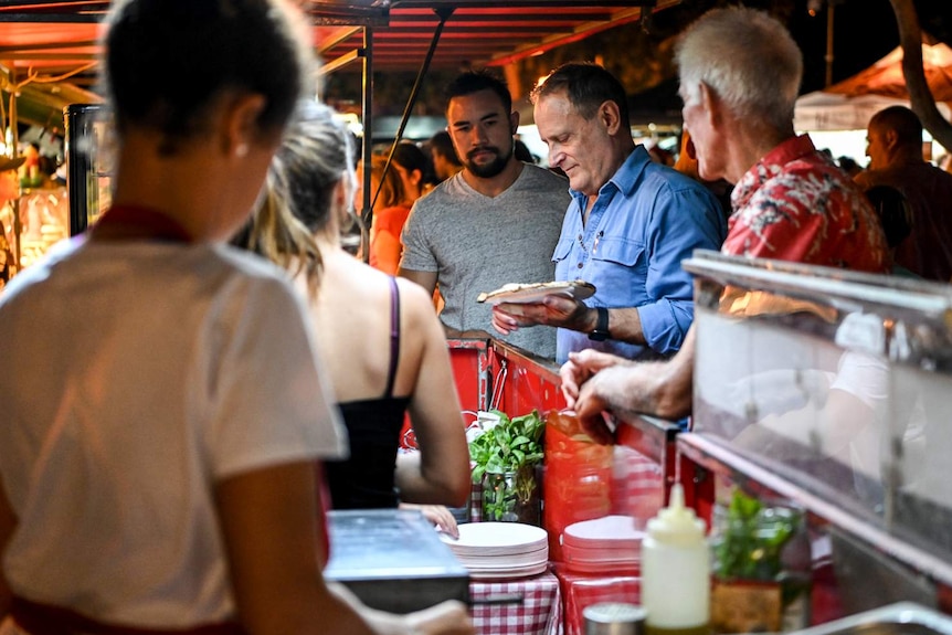 Three men stand around a food stand.