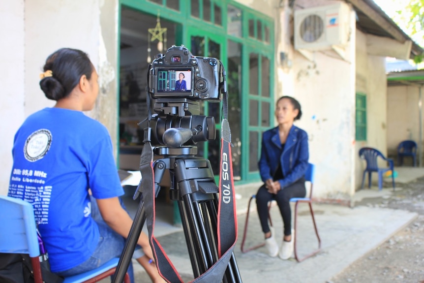 An EOS 70D camera on a tripod filming two women in a seated interview.