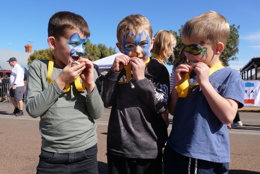 three young boys with painted faces bite gold medals