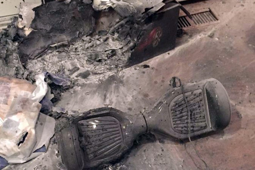 A charred toy hoverboard with fire-damaged packaging and floor.