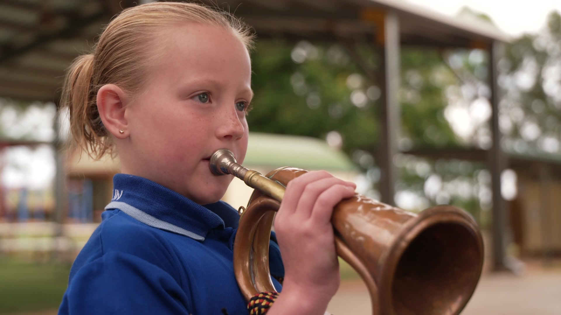Close-up photo of a young girl playing the bugle. She is wearing a blue school uniform.