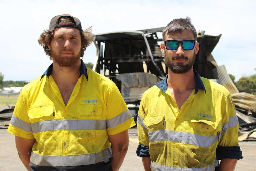 Two men in high-vis shirts standing in front of the wreckage.