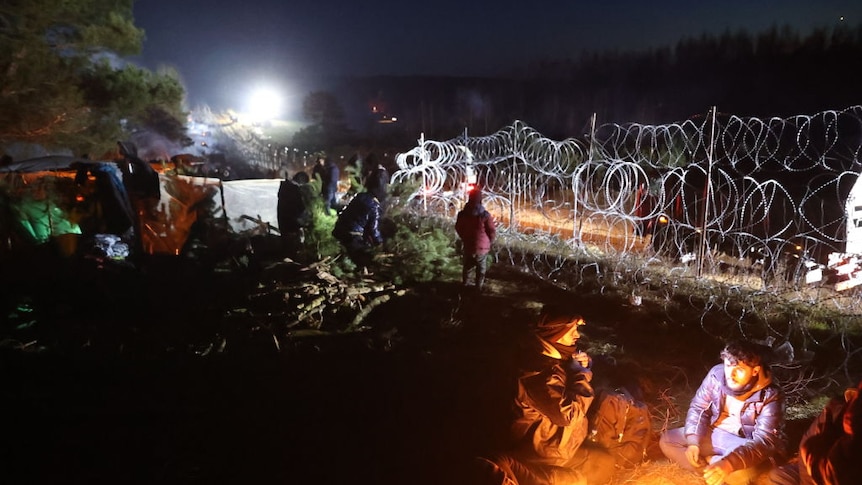 A night time photo of migrants camped at the Polish-Belarusian border with razor wire in the background