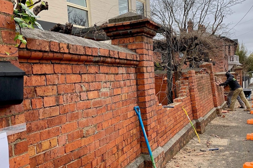 A partly demolished red brick fence, at a construction site.