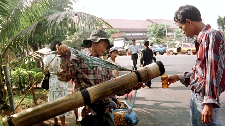 An Indonesian man selling fermented coconut palm wine serves his customer from a bamboo tube.