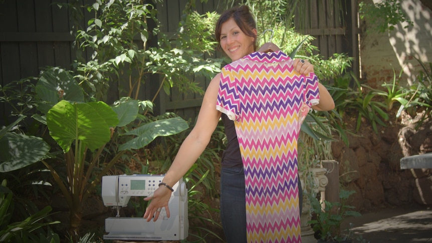 Tamara DiMattina in a garden holding a dress with a sewing machine next to her.