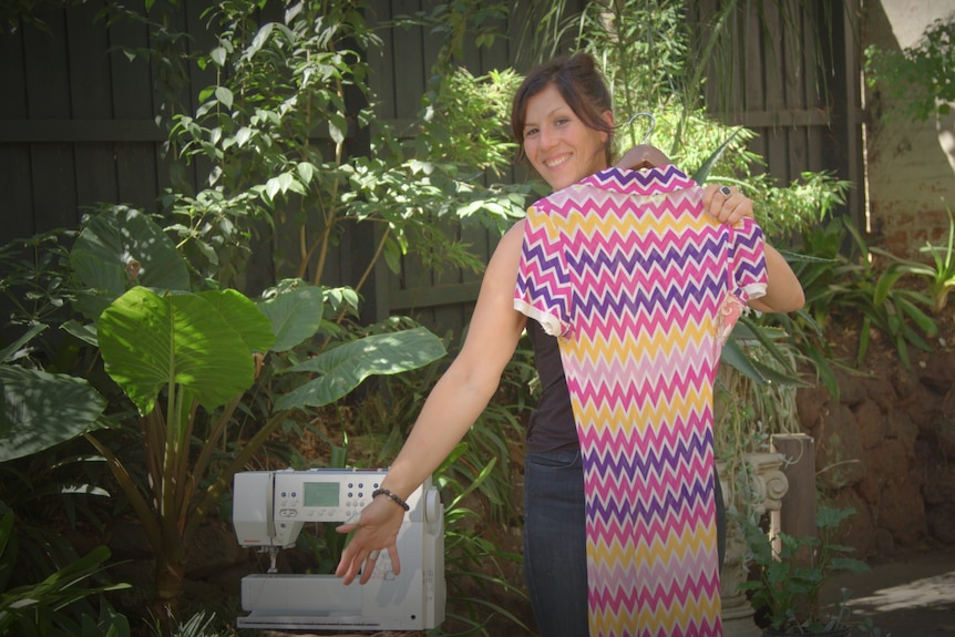 Tamara DiMattina in a garden holding a dress with a sewing machine next to her.