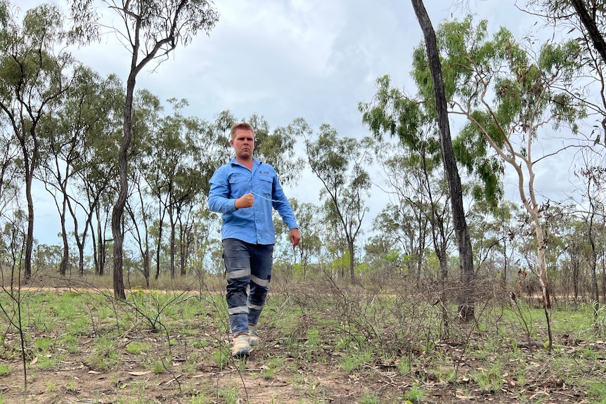 Roman Dubinchak in light blue workshirt and work pants holds two rods as he water divines through bushland