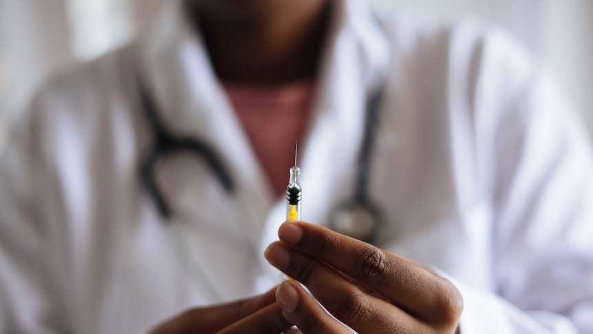 Doctor wearing white lab coat holds vaccine out in front of her.