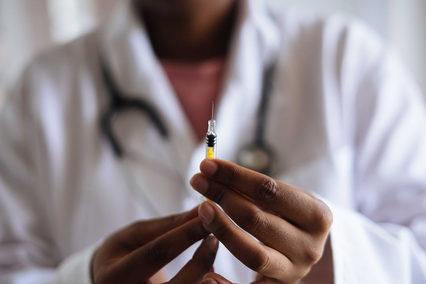 A man wearing a blue face mask holds up a vial of experimental COVID-19 vaccine.