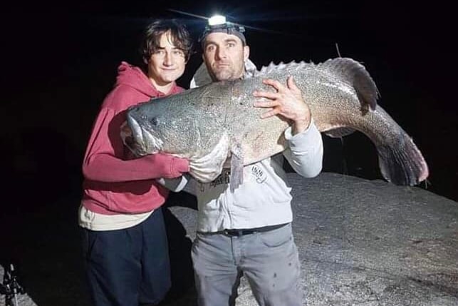 Two men hold up a fish in the dark