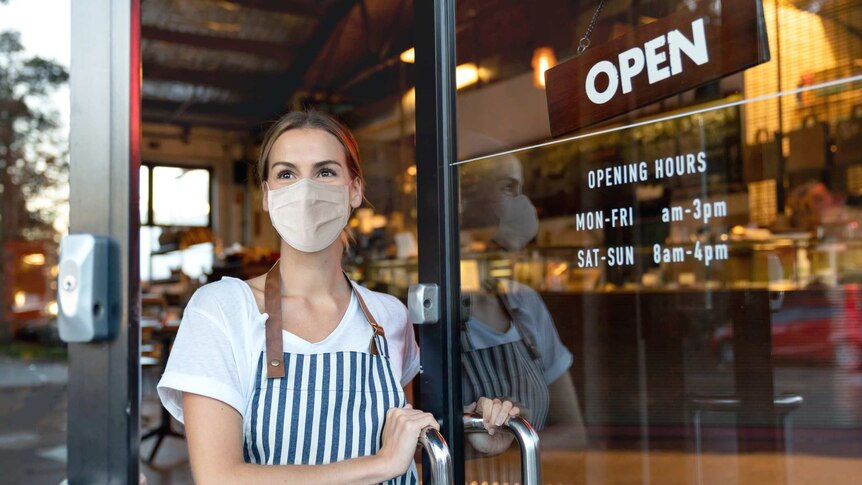 Happy business owner opening the door at a cafe wearing a facemask