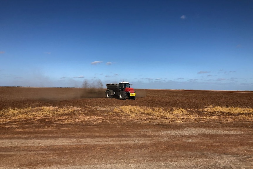 A spreader puts compost back onto a brown, bare cotton field.