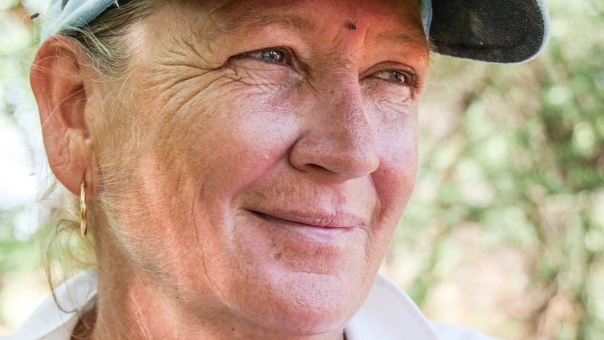 A smiling woman in a white linen shirt and a cap stares out of shot.