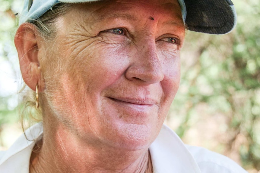 A smiling woman in a white linen shirt and a cap stares out of shot.