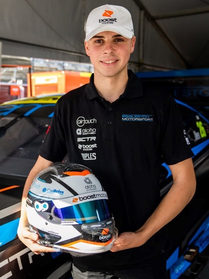 Young an wearing cap in front of a blue racing car