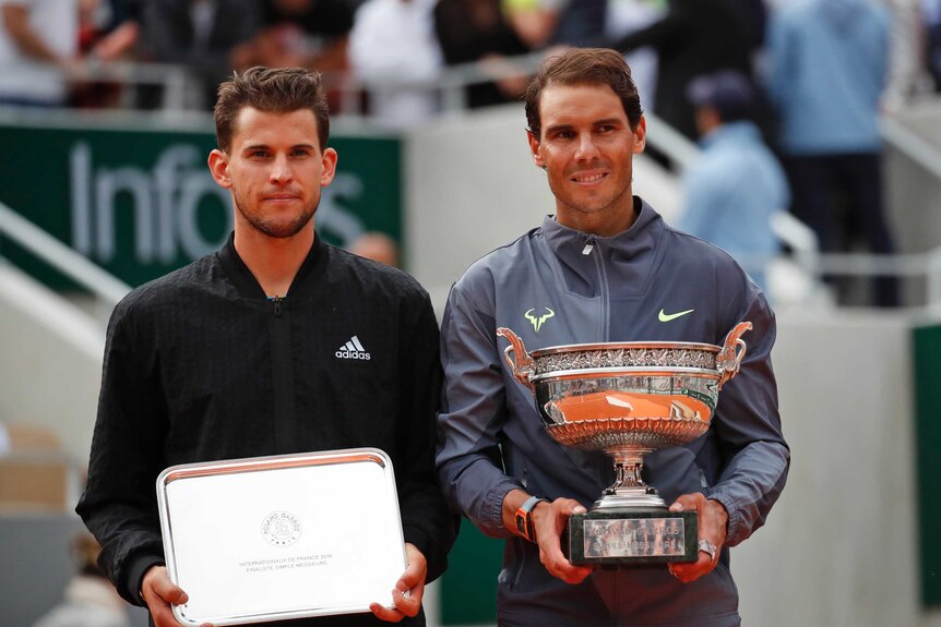 Rafael Nadal holds his trophy as he stands next to Dominic Thiem, who holds his second-place tray