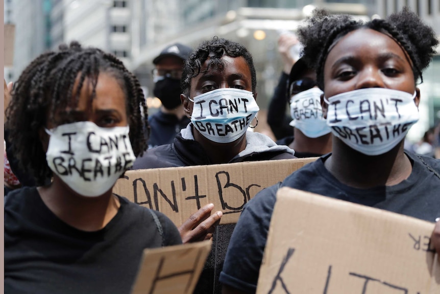 Three people stare at the camera with signs and masks reading "I can't breath".