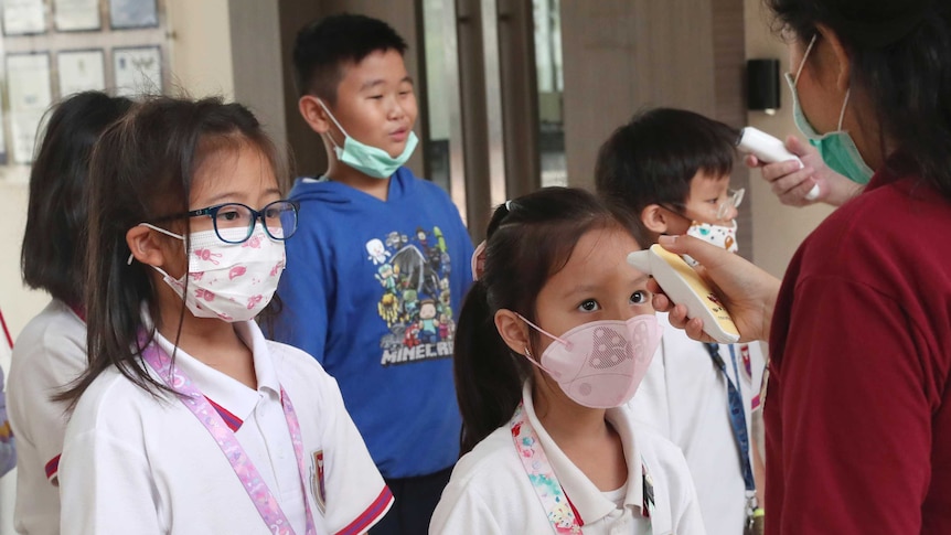 Indonesian school students wearing protective face masks have their temperature taken