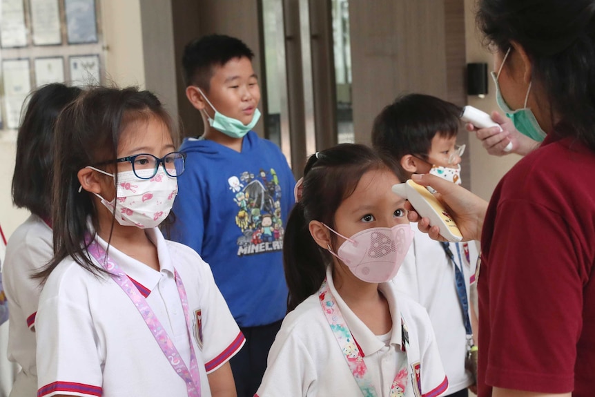 Indonesian school students wearing protective face masks have their temperature taken