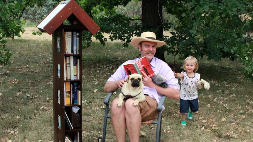 Patrick Dillon, 2-year old Charlotte Marsh and Pudding the pug at the Little Free Library in O'Connor, ACT.