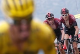Aliphilippe, wearing the yellow jersey, is out of focus in front. Poels and Thomas, wearing red, grimace as they ride behind