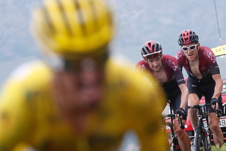 Aliphilippe, wearing the yellow jersey, is out of focus in front. Poels and Thomas, wearing red, grimace as they ride behind