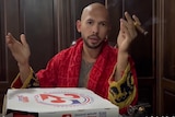 A bald man in a bath robe smoking a cigar with a pizza box in front of him