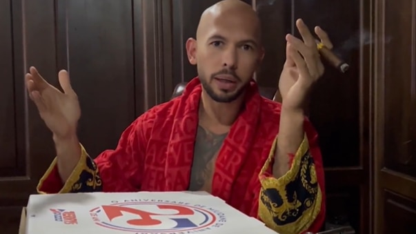 A bald man in a bath robe smoking a cigar with a pizza box in front of him