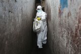 A health worker in Ebola protective clothing carrying a white bag.