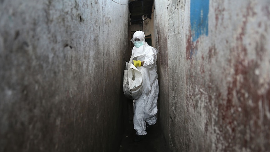 A health worker in Ebola protective clothing carrying a white bag.