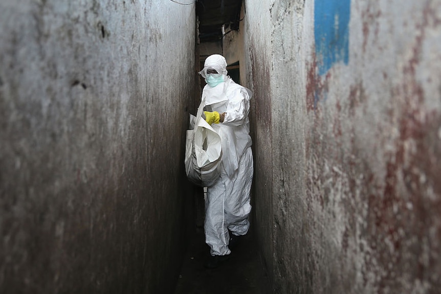 A health worker in Ebola protective clothing carrying a white bag.