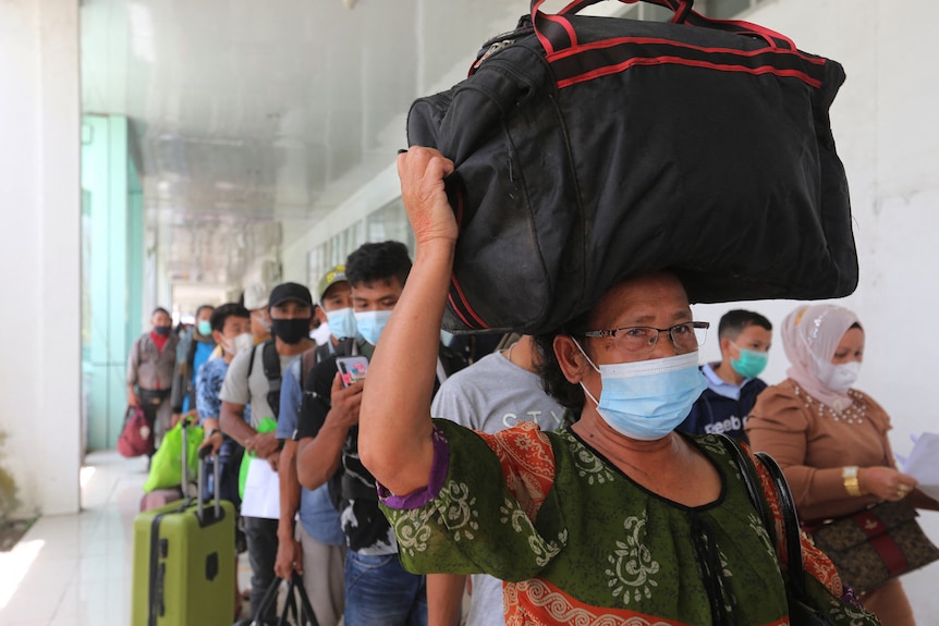 A woman carries a bag on her head among passengers wearing face masks