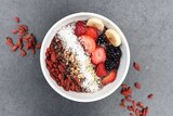 A bowl filled with a smoothie and topped with fruit and coconut, with goji berries alongside.