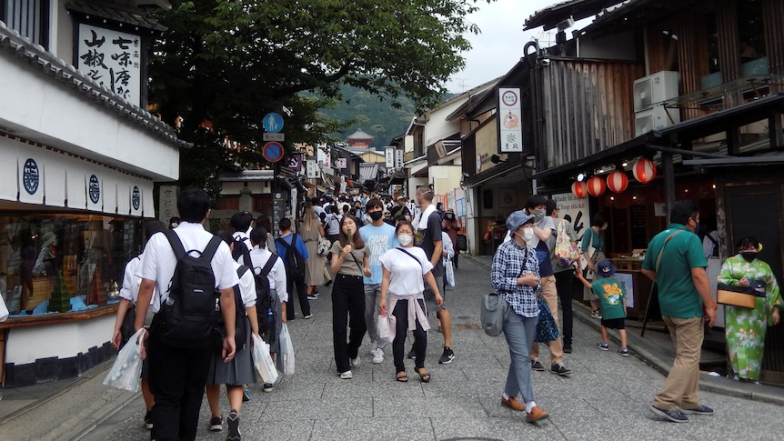Mostly masked people walk along roads between old Japanese buildings