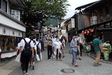 Mostly masked people walk along roads between old Japanese buildings