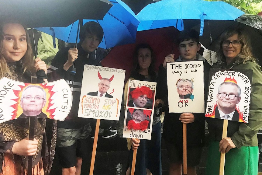 Protesters hold umbrellas in the rain holding placards at Melbourne climate rally.