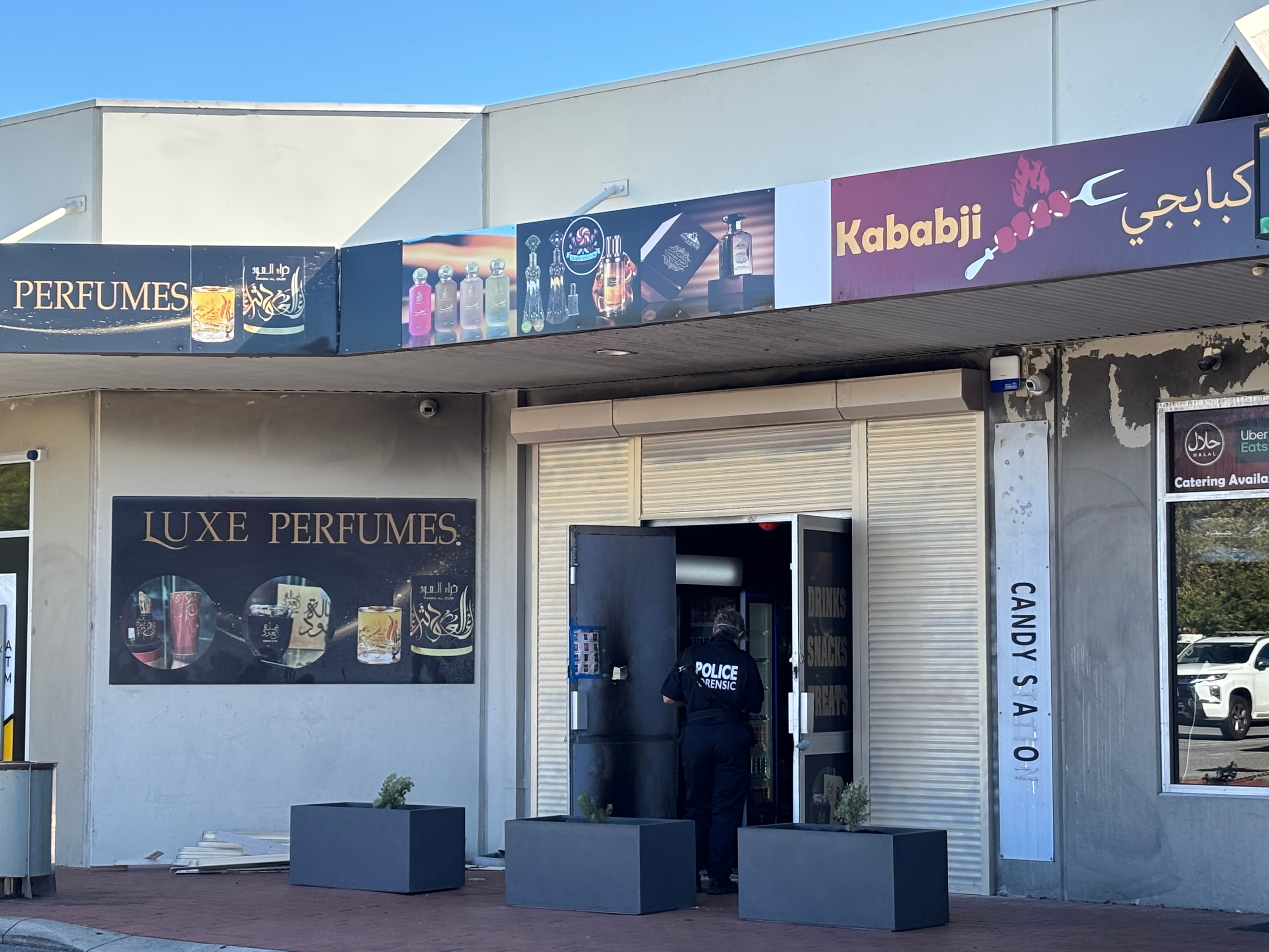 Un oficial forense de la policía se encuentra frente a una pequeña tienda con un cartel de perfume en el frente.