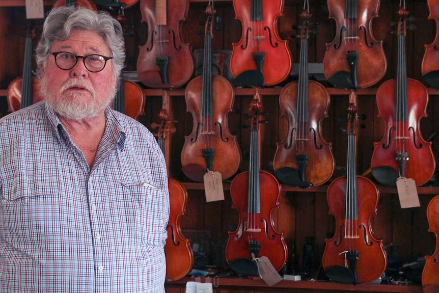 Farmer and musician Allan Walsh stands in front of violin colelction