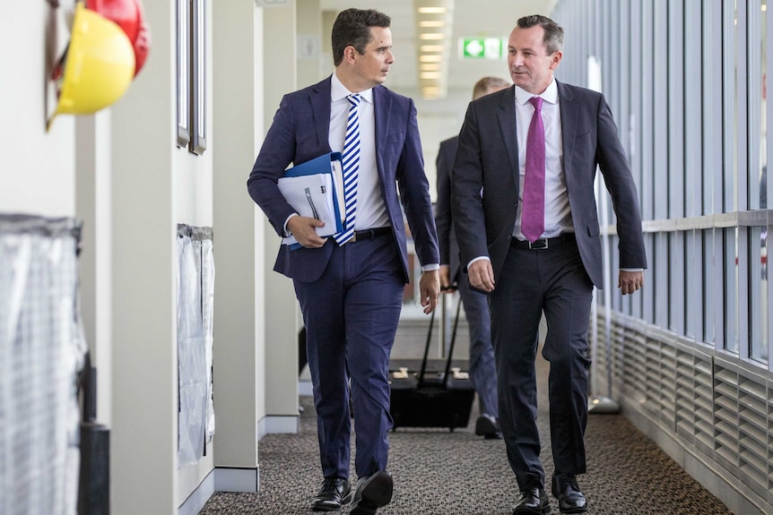 WA Treasurer Ben Wyatt and Premier Mark McGowan walk down a hallway talking to one another wearing suits and ties.