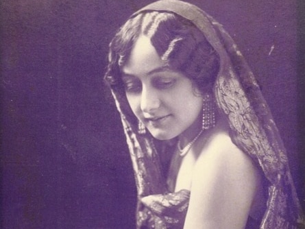 A black and white photograph of a woman wearing earrings and a head covering looking over her shoulder.