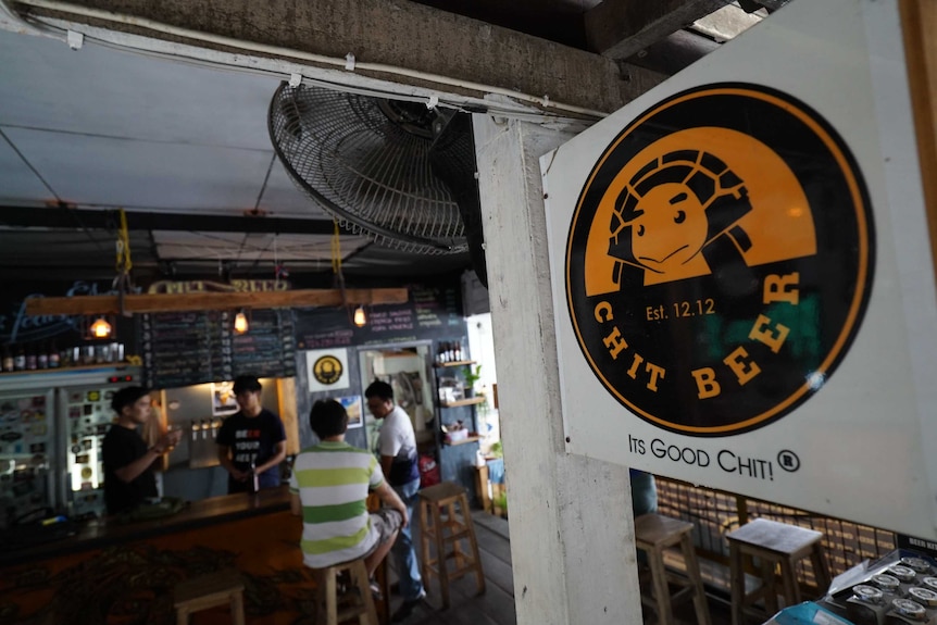 Out of focus picture from a distance of people inside the Chit's bar with a close up of a sign saying Chit Beer, It's good chit!