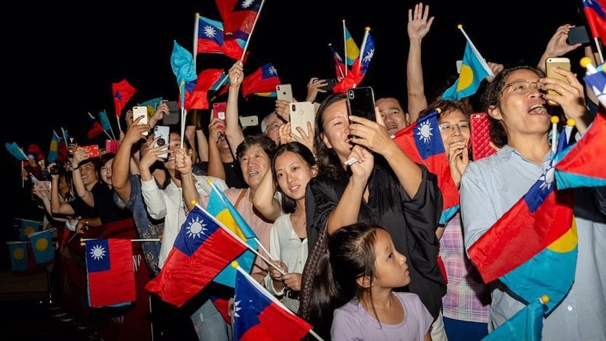 A group of people waving Taiwan and Palau flags and taking photographs.