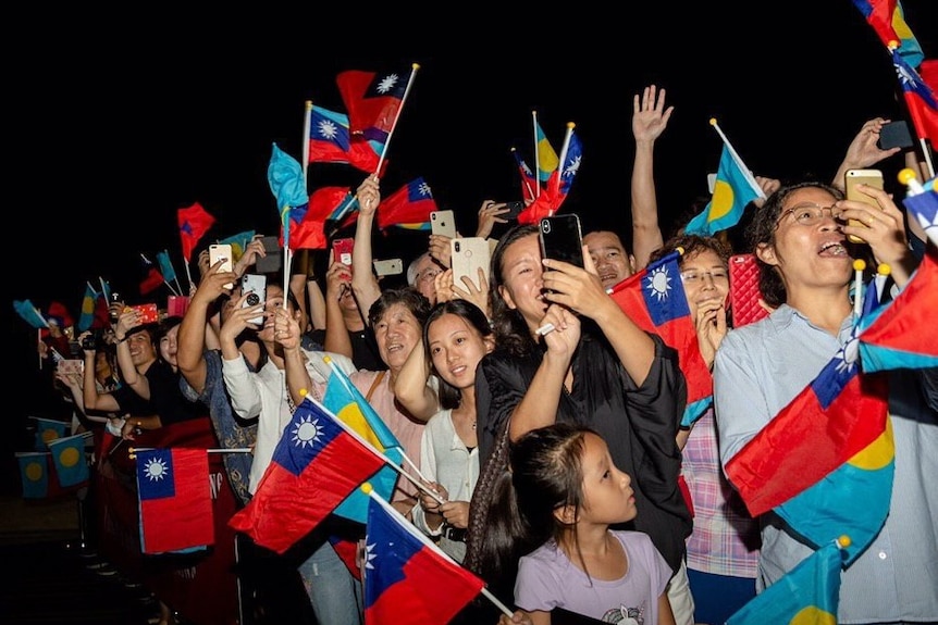 A group of people waving Taiwan and Palau flags and taking photographs.