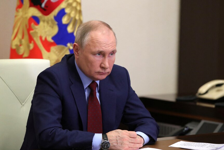 Vladimir Putin sits with hands clasped together.