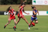 A woman in a red uniform kicking an aussie rules ball