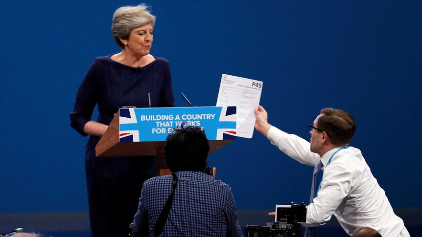 An audience member approaches the podium to hand Ms May a piece of paper.