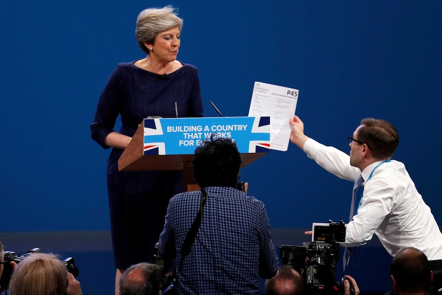 An audience member approaches the podium to hand Ms May a piece of paper.