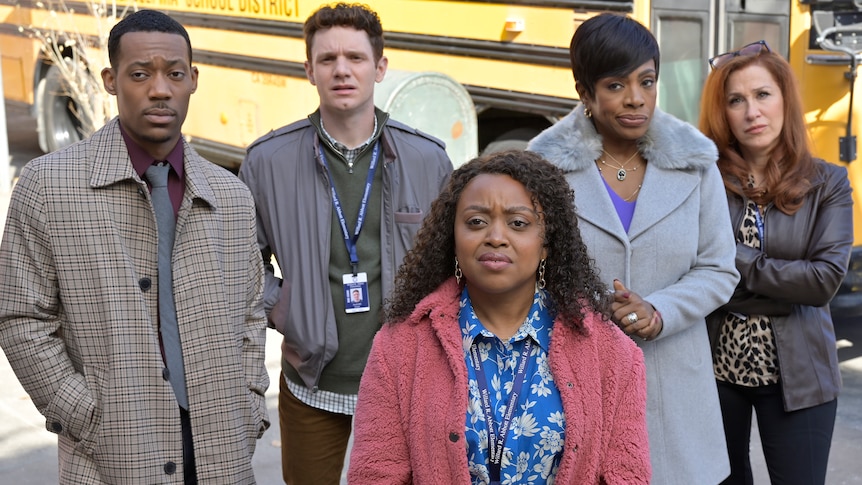 A black man in a trench coat, white man in a bomber, a black woman in cardigan, a black woman in coat and white woman in jacket.